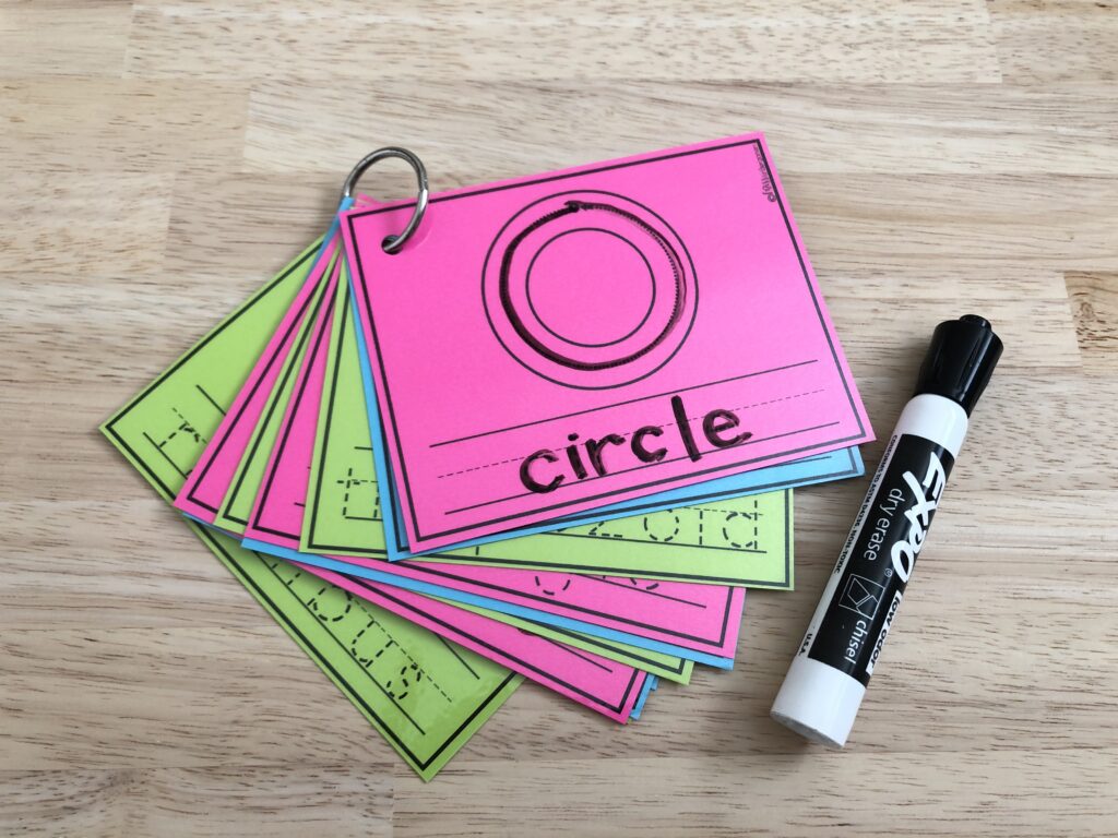 A stack of shape tracing cards have been added to a binder ring and are being used with a dry-erase marker as a 2D shape activity.