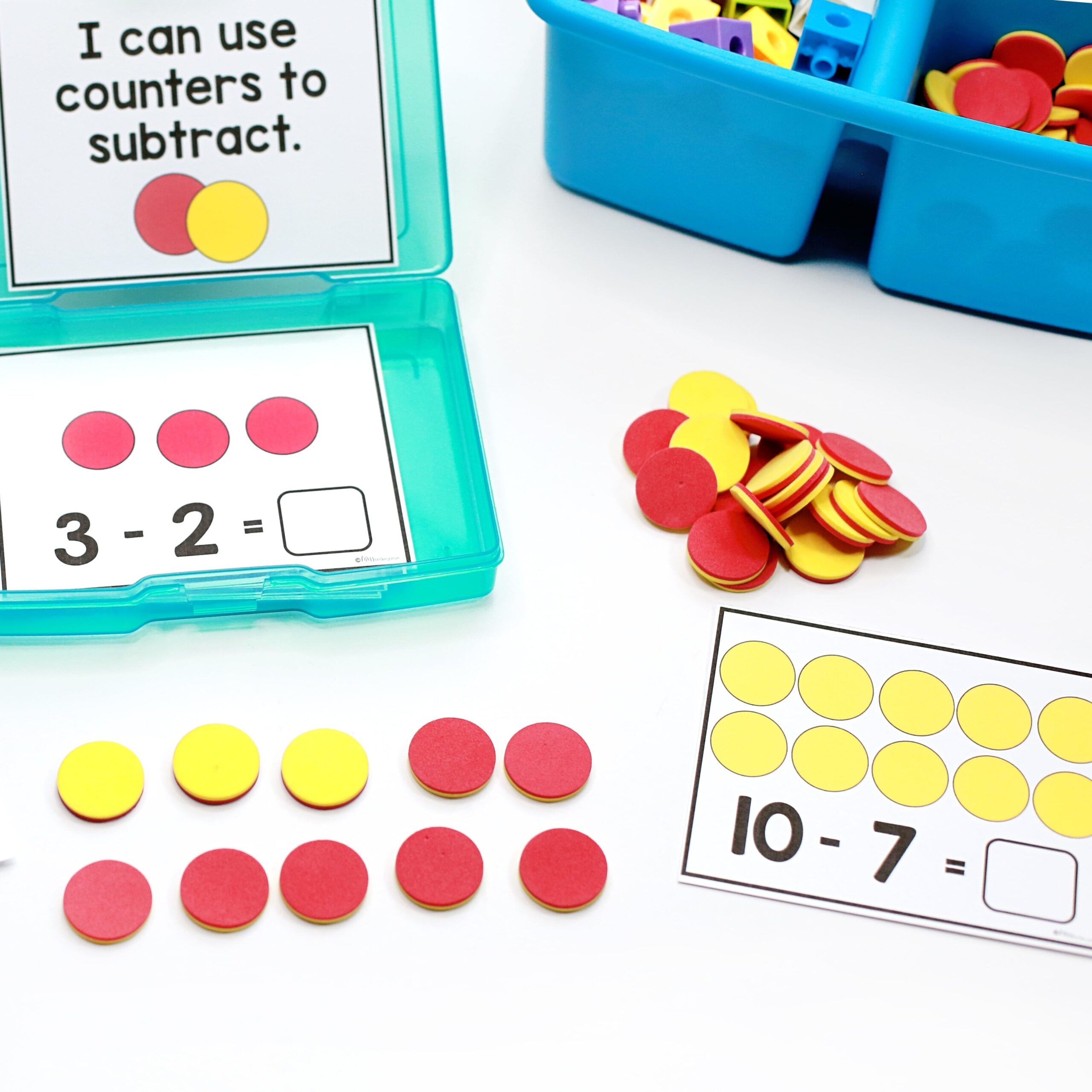 A white desk top with a container of subtraction task cards, one task card in use, and a pile of two-color counters being used to model the subtraction equation.