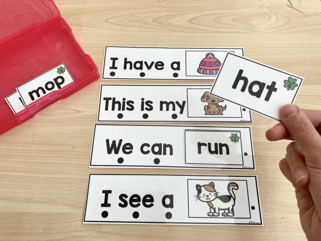 Multiple sight word sentence strips are in use, with a student hand placing a card on an additional sentence card.