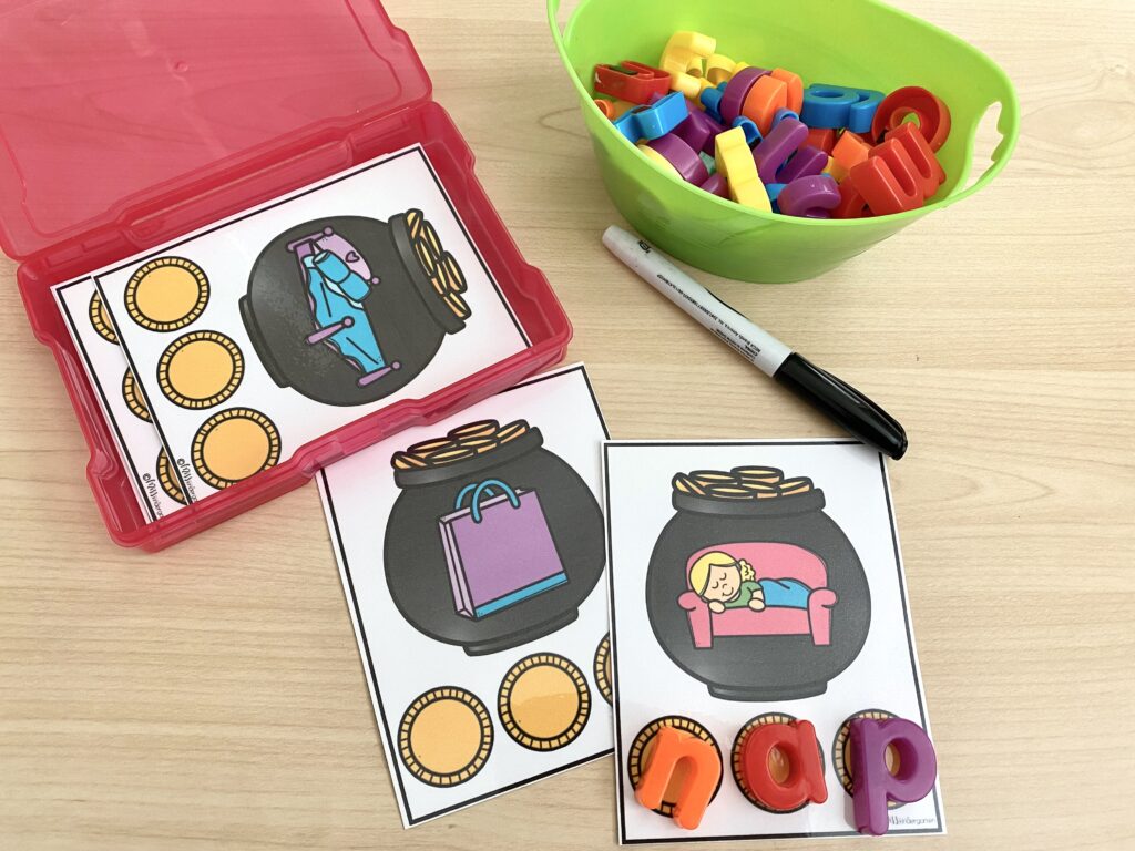 A cvc word building activity is being used on a desk. A bin of magnetic letters and marker are also on the desk. Magnetic letters have been added to spell a word to match the image shown on a pot of gold.