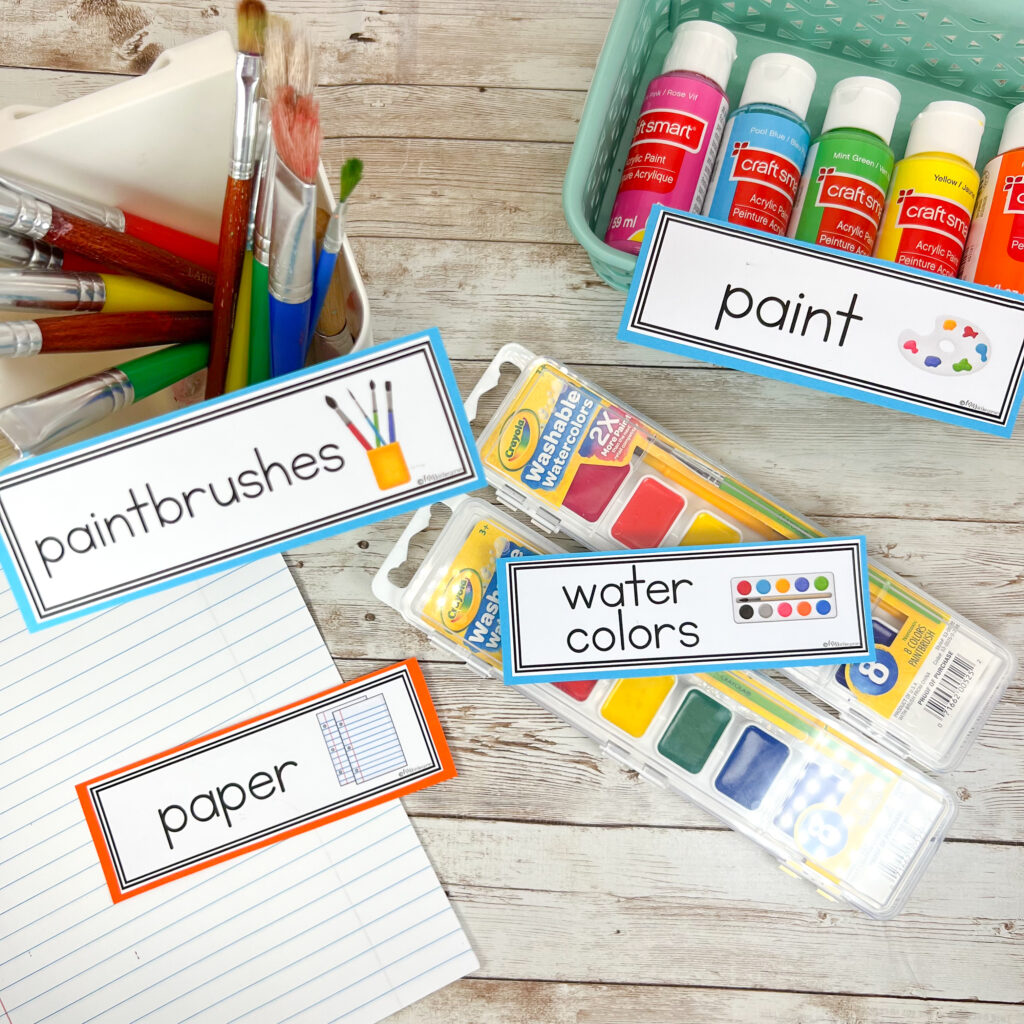 Paint, paper, and paintbrushes labeled with classroom labels